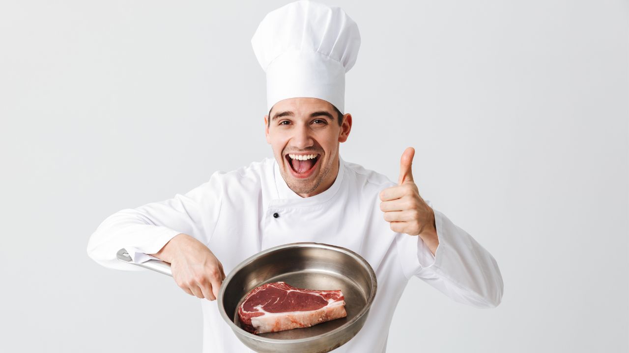 chef holding a pan with a steak and doing a thumbs up