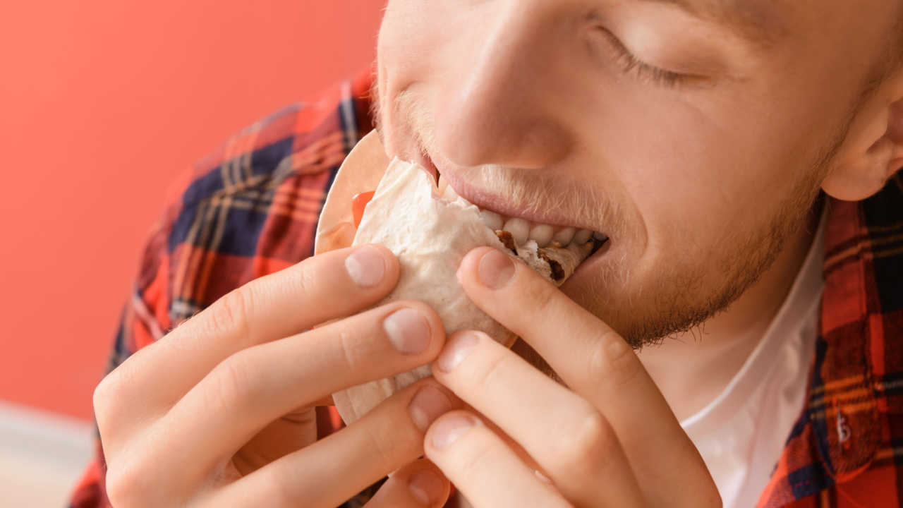 man happily eating food, has a wrap in his mouth