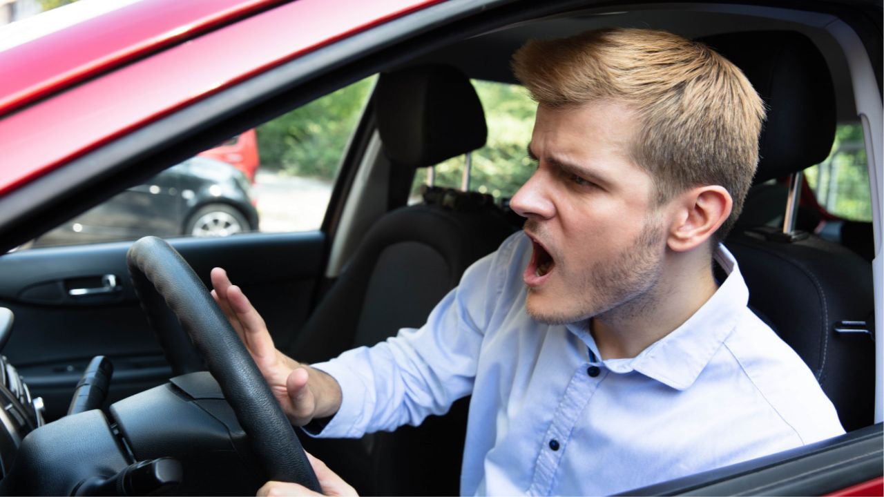 man sitting in car honking horn, looking angry
