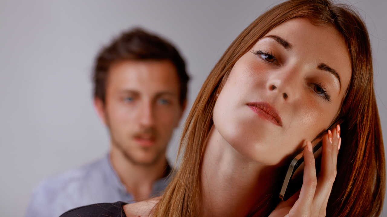 woman angry talking on phone while man watches from behind