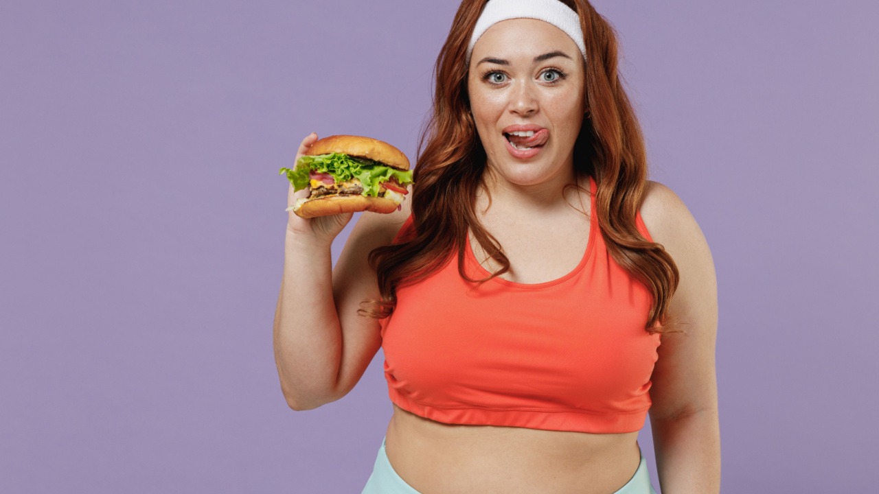 woman holding a burger while wearing a headband and workout clothes