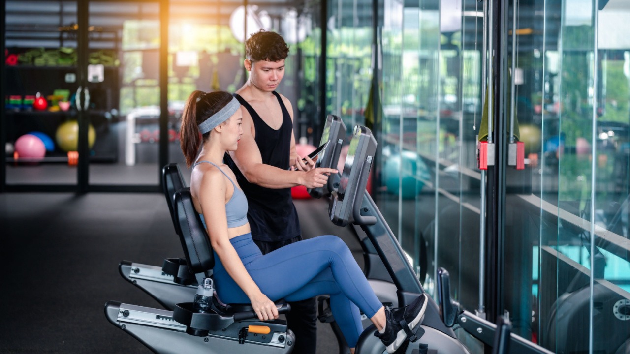 woman sitting on an exercise bike whle man coaches at the gym