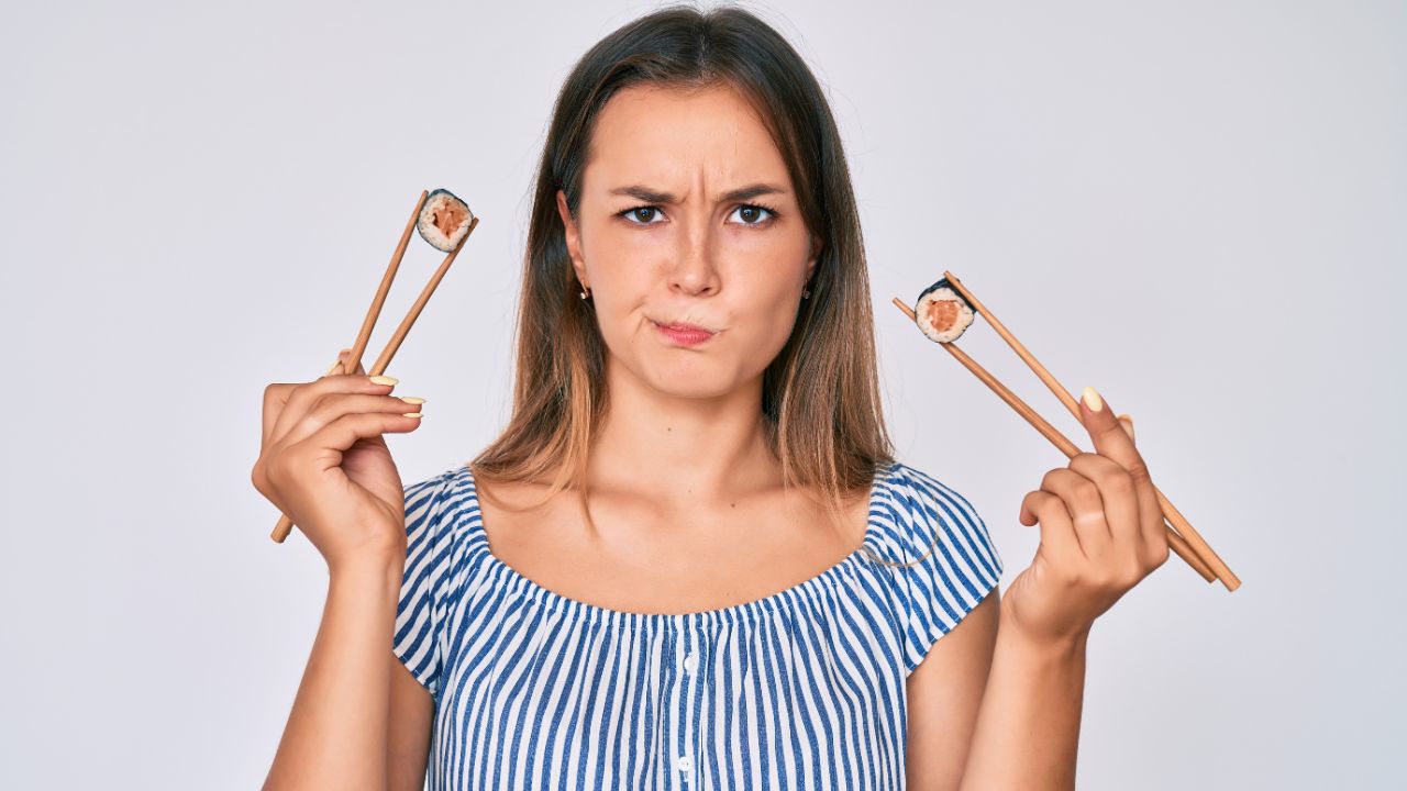 woman with chopsticks in each hand holding sushi