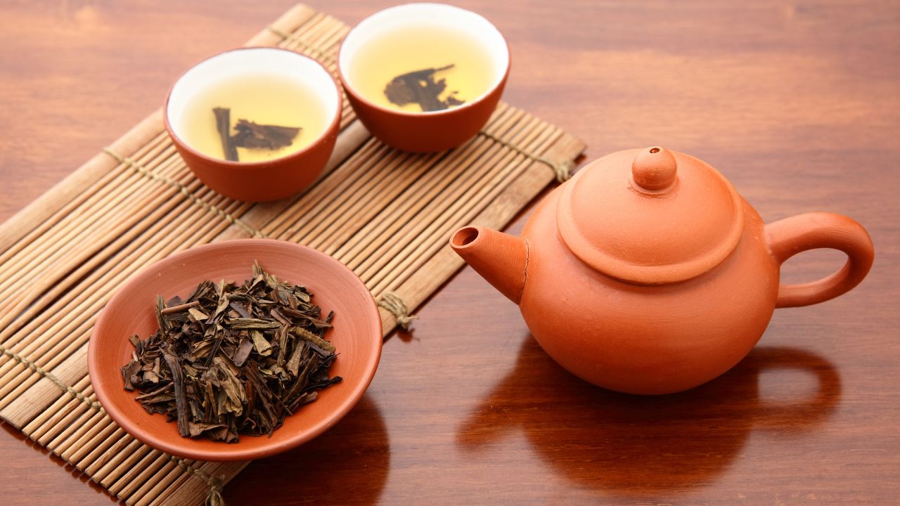 teapot beside a bowl of tea leaves and two other bowls with tea
