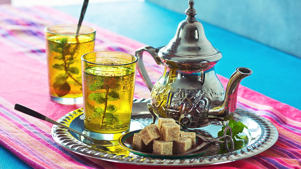 Moroccan tea in a kettle and two glasses with sugar cubes on a plate