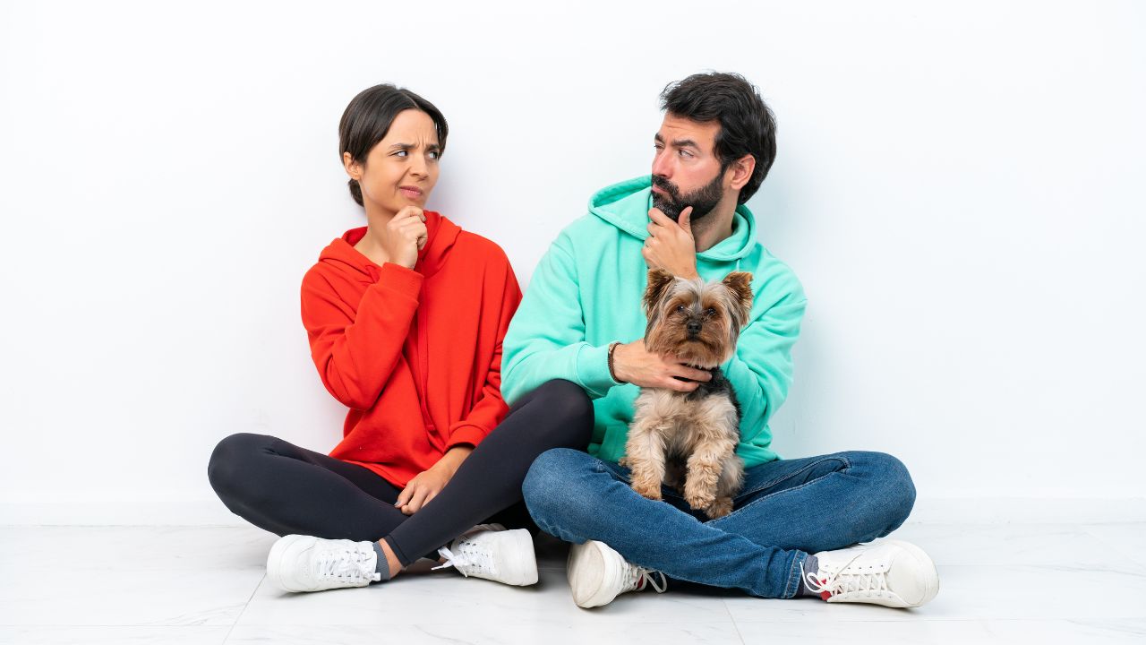 man holding dog sitting beside woman, both looking at each other