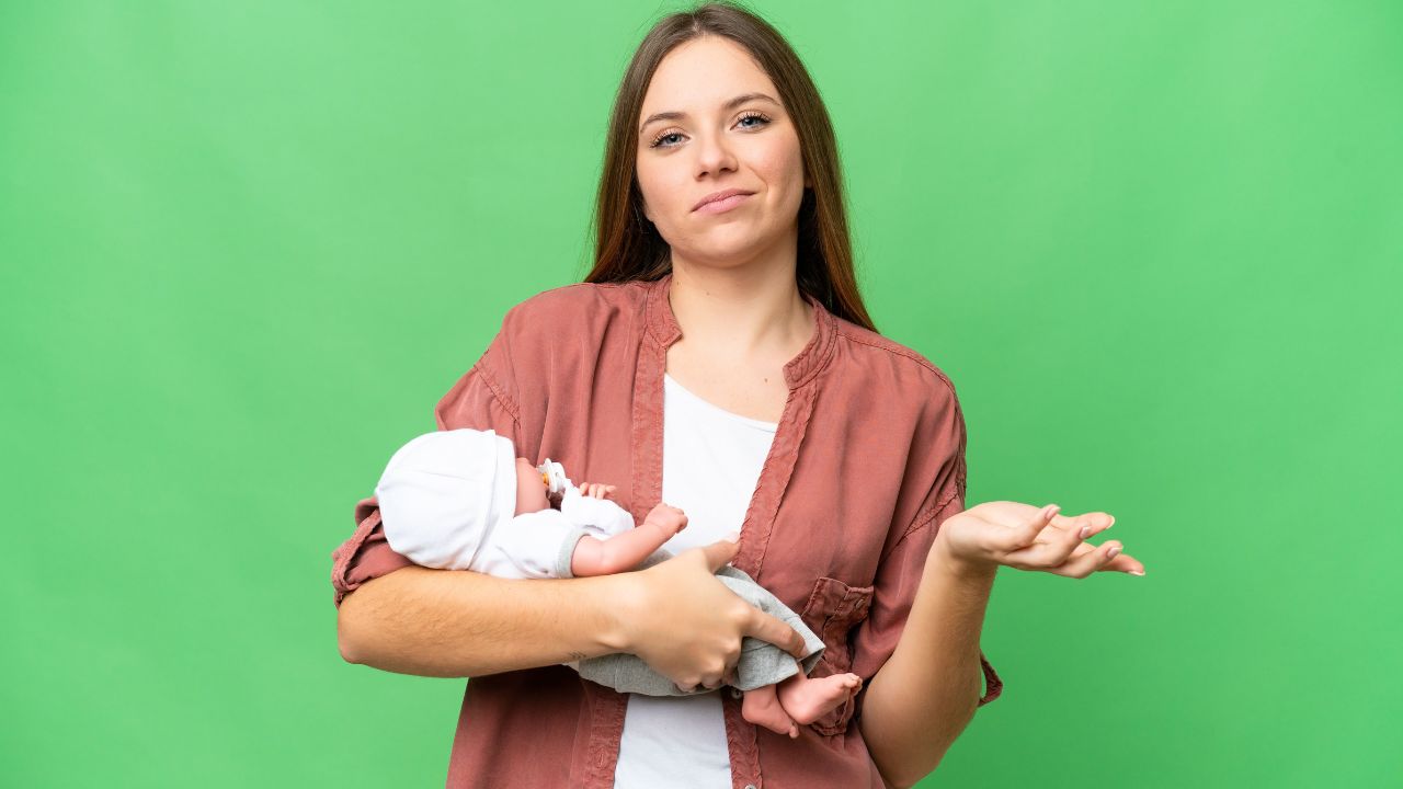 woman holding a baby doll and looking confused with hand up