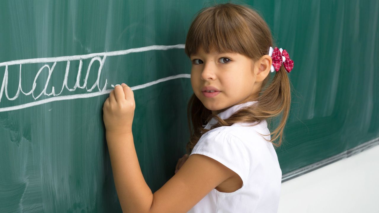 girl standing in front of chalk board at school writing in cursive with chalk