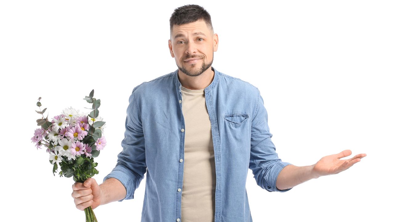 man holding flowers with arms out looking apologetic but confused