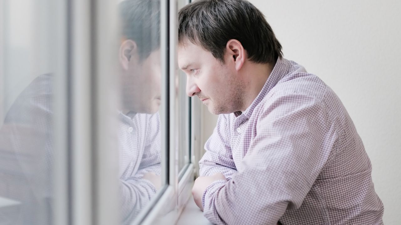 man looking out of window, looking sad and grieving