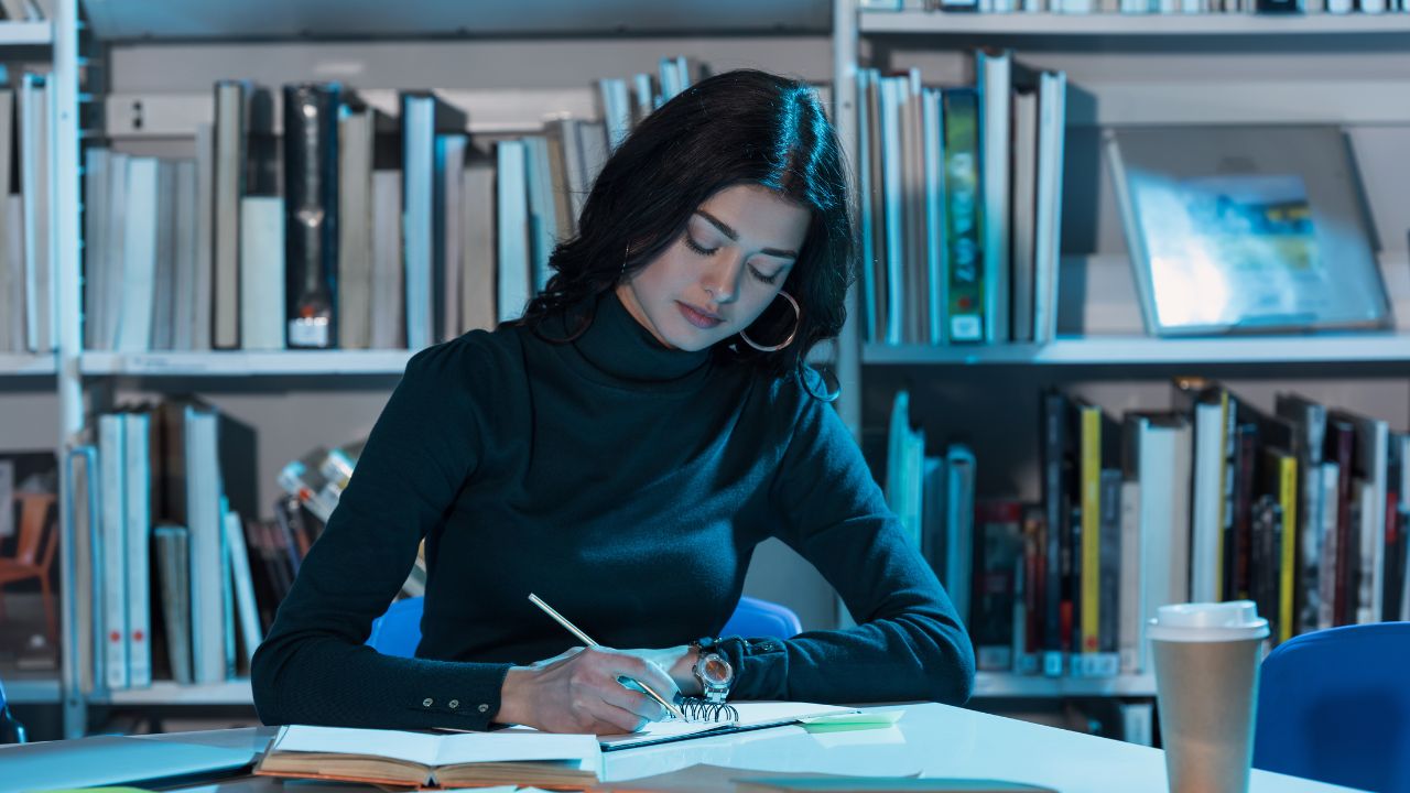 student sitting at table in library writing notes