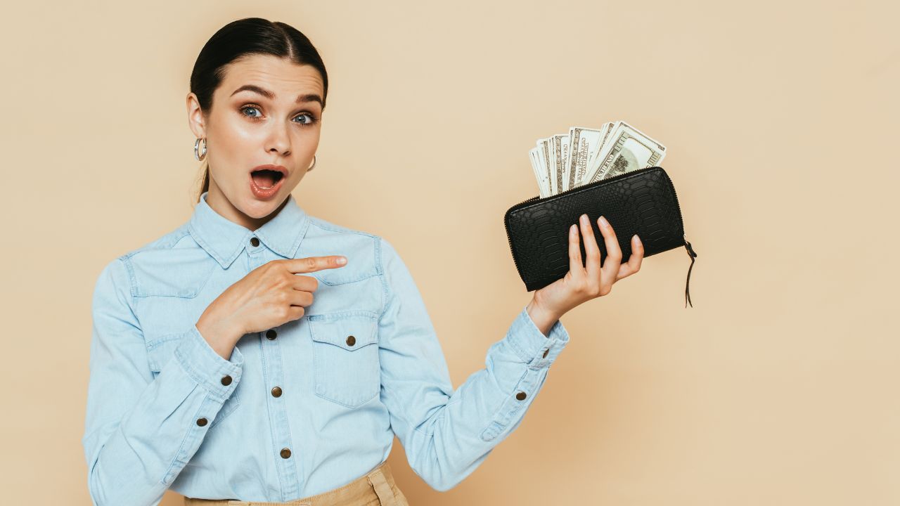 woman holding wallet with money and pointing at it looking surprised