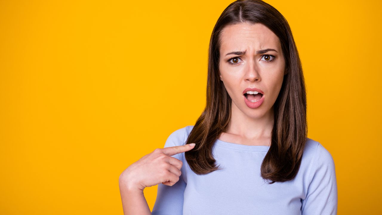 woman pointing to herself looking confused she is being blamed