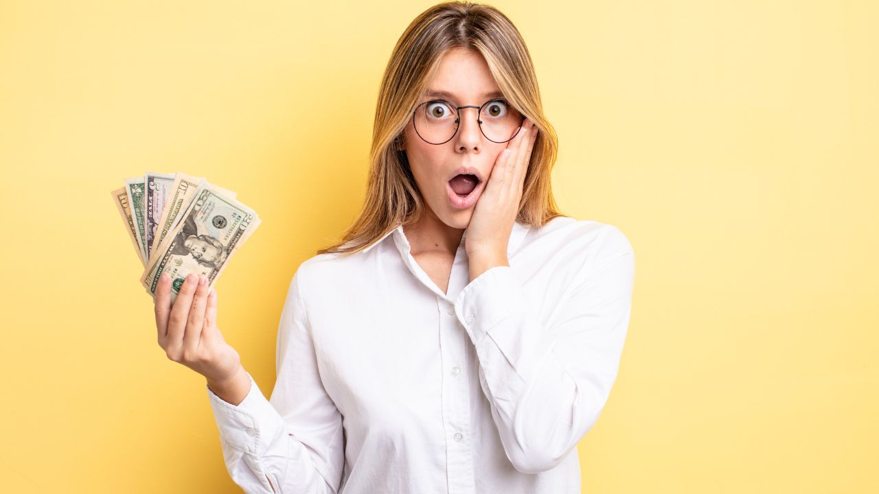 woman looking upset and shocked with hand on face and holding money in other hand