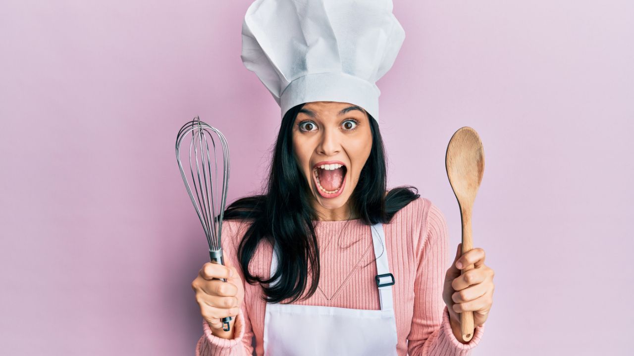 woman wearing chef's hat and holding baking tools, looking happy and crazy