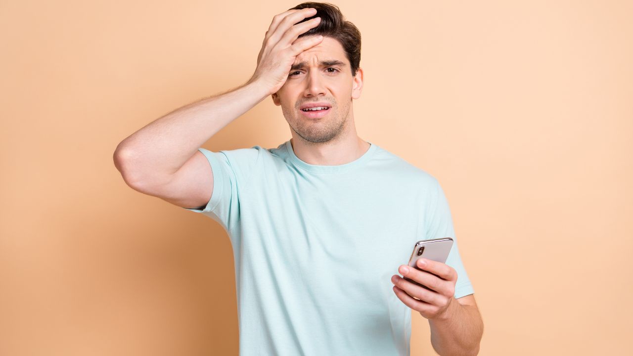 man with hand on forehead while looking at phone