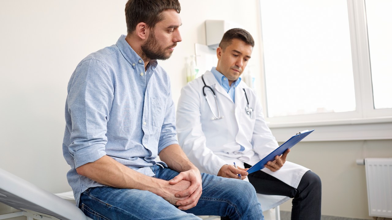 man sitting beside male doctor looking at a clipboard during an appointment