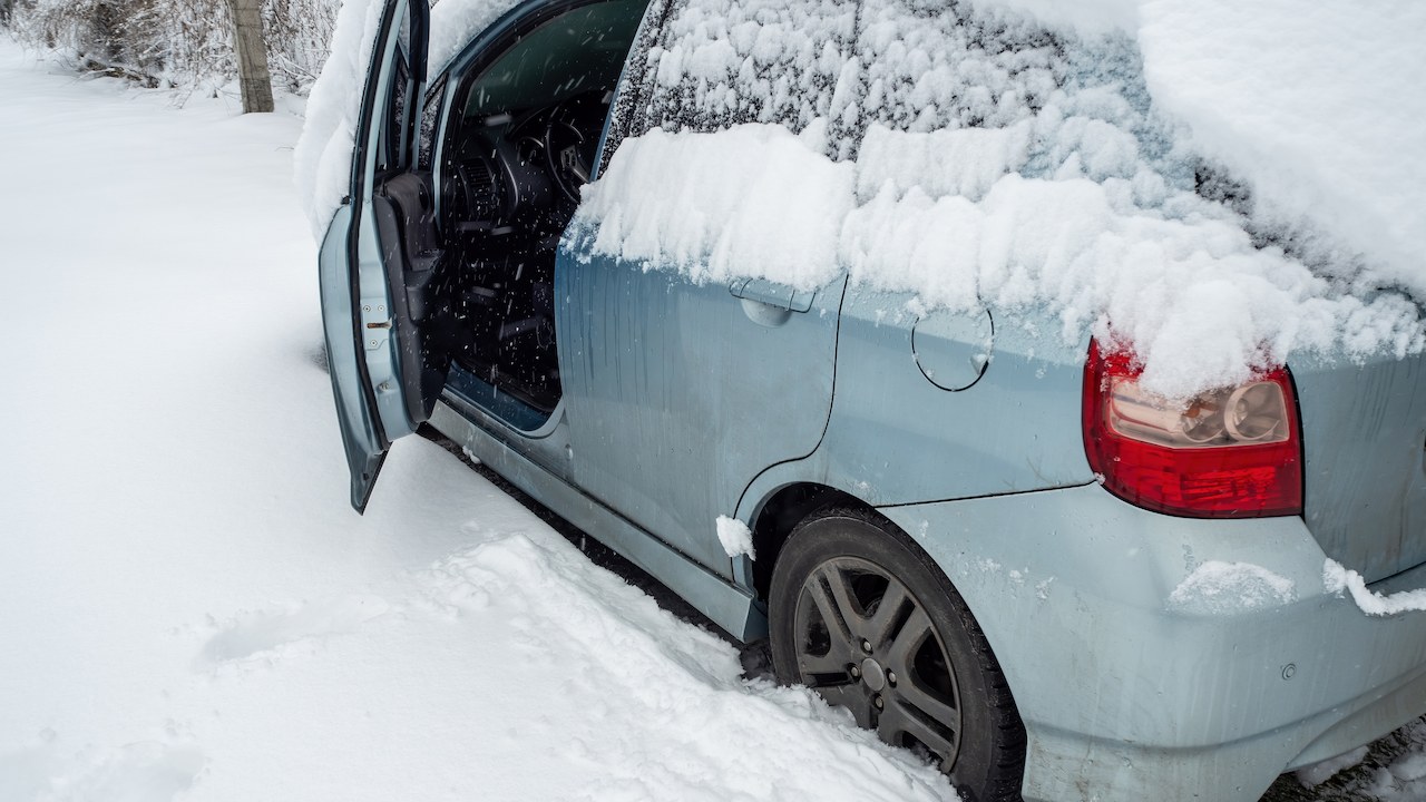 car with door open, sitting in a lot of snow and snow piled on top of the car.