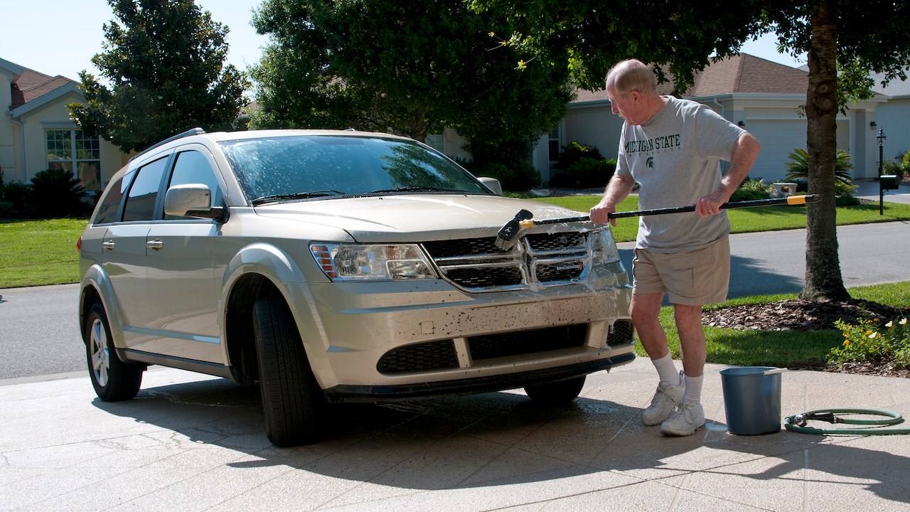 man cleaning front of his car, cleaning bugs off of his car