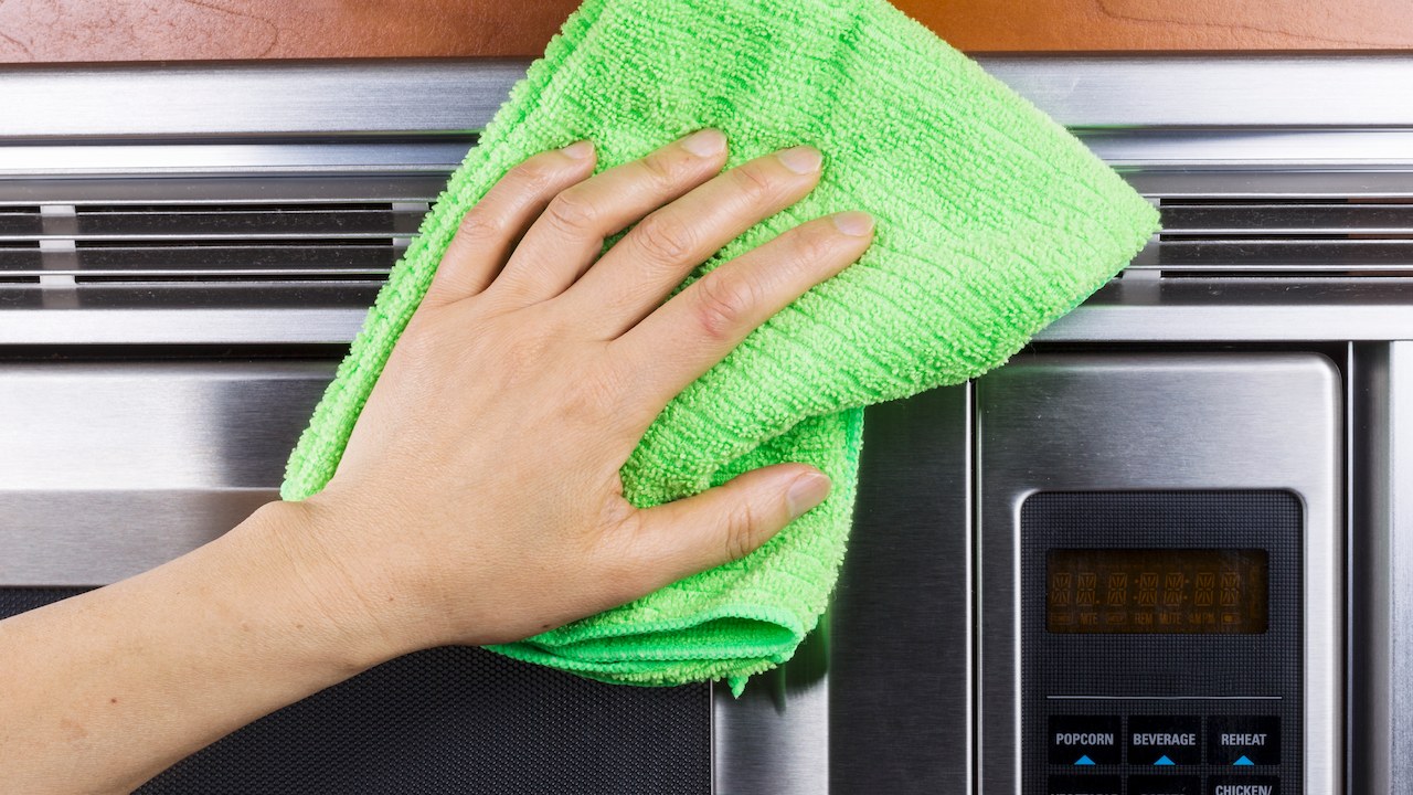 person wiping a stainless steel microwave with a microfibre cloth