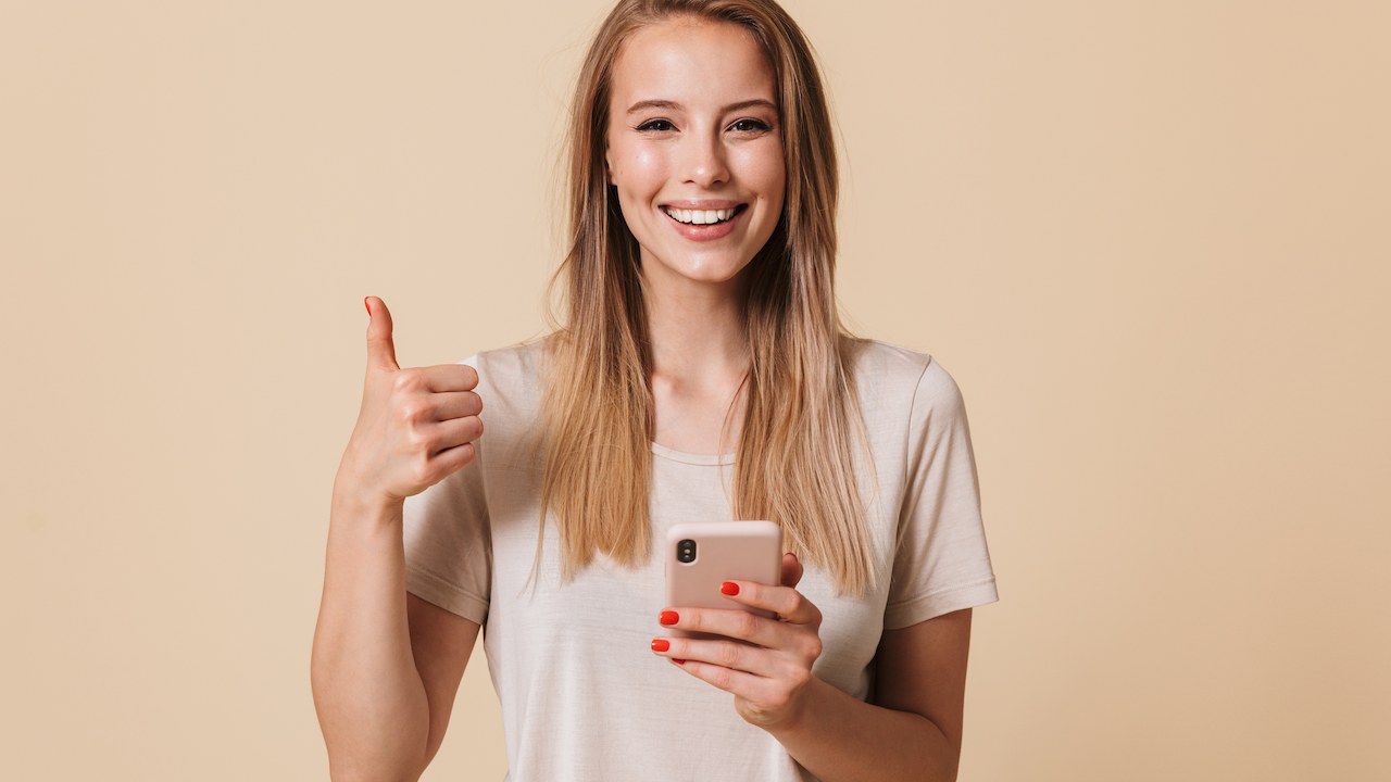 woman holding a phone while making a thumbs up gesture and smiling