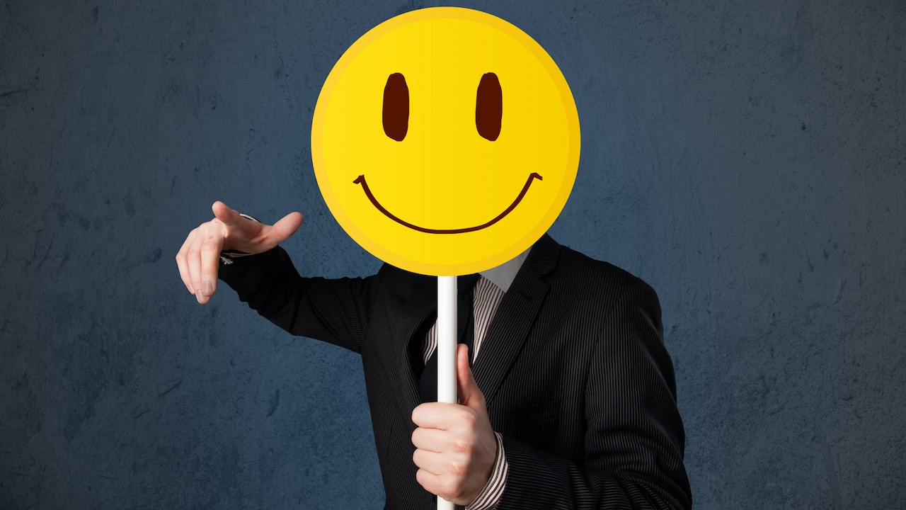 A man holding a yellow smiley face props covering his face