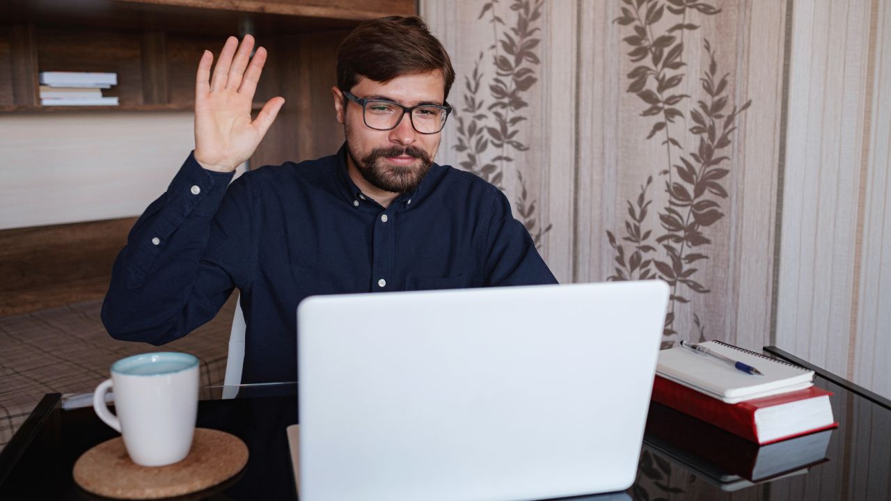 GenZ man waving in front of laptop, zoom call