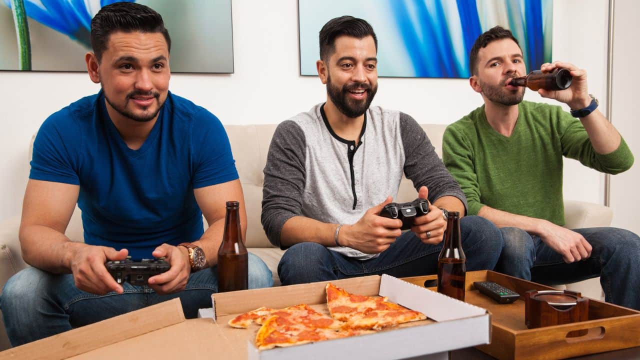 three men playing video games and eating pizza